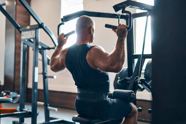 Adult bodybuilder doing heavy weight exercise for back on machine while in gym. Bodybuilding concept - Photo, image
