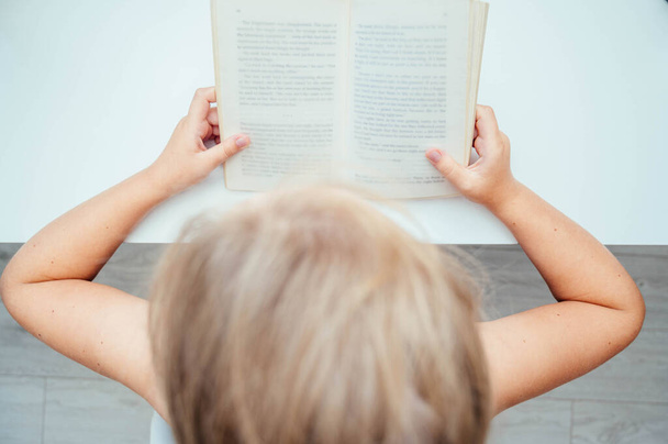 Вид зверху на маленьку дівчинку, що читає книжку. Домашня освіта, концепція дистанційного навчання
 - Фото, зображення