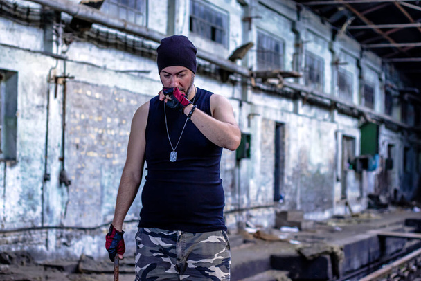 Young rebel in abandoned factory hall with a metal bar in his hand. Selective focus. - Valokuva, kuva