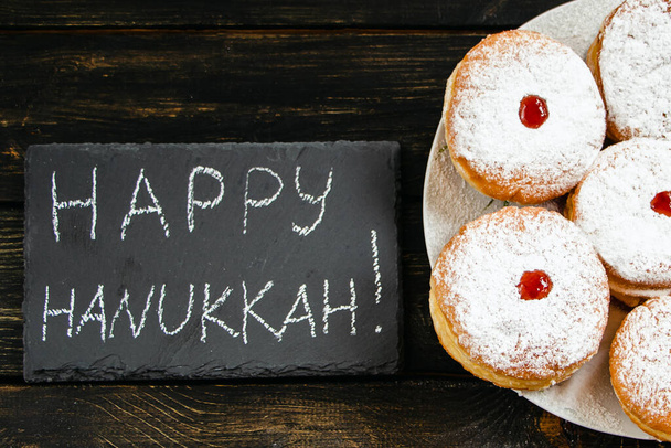 Feliz Hanukkah. Sobremesa tradicional Sufganiyot em fundo de madeira escura. Donuts, velas e presentes. Celebrando feriado religioso judaico. - Foto, Imagem