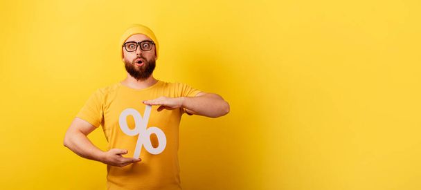 shocked man hold 3d percentage sign over yellow background, discounts with high interest, panoramic layout with space for text - Photo, Image