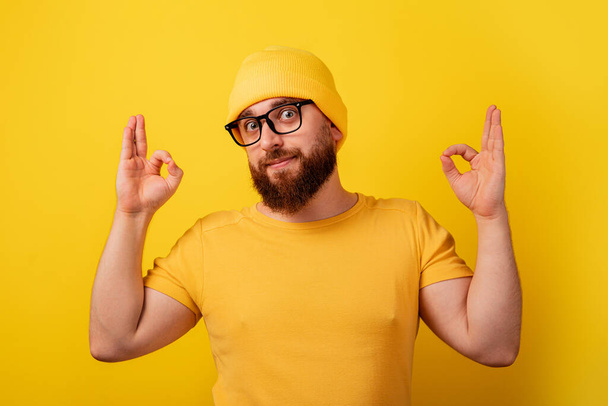 homme barbu dans des lunettes montrant ok geste sur fond jaune - Photo, image
