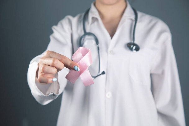 arts houdt een roze lint in zijn hand op een grijze achtergrond - Foto, afbeelding