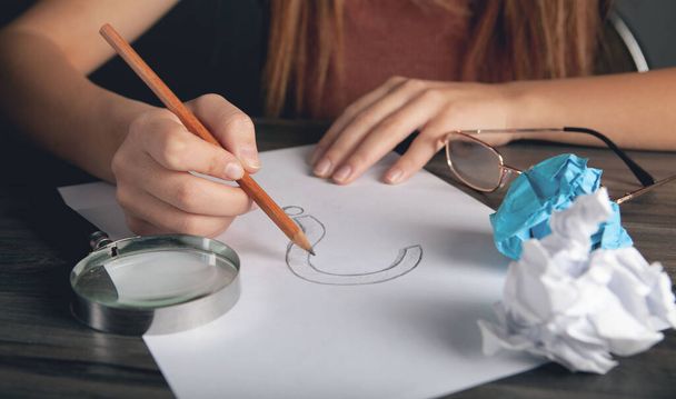 Frau zeichnet Fragezeichen auf Papier und neben einer Lupe - Foto, Bild