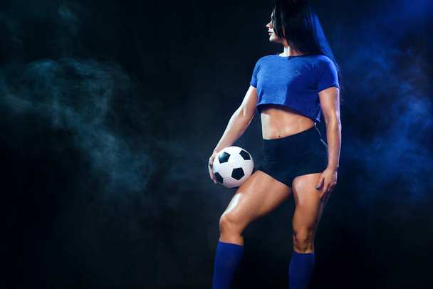 Strong athletic woman with soccer ball on black background. Sport concept. Football fan. - 写真・画像