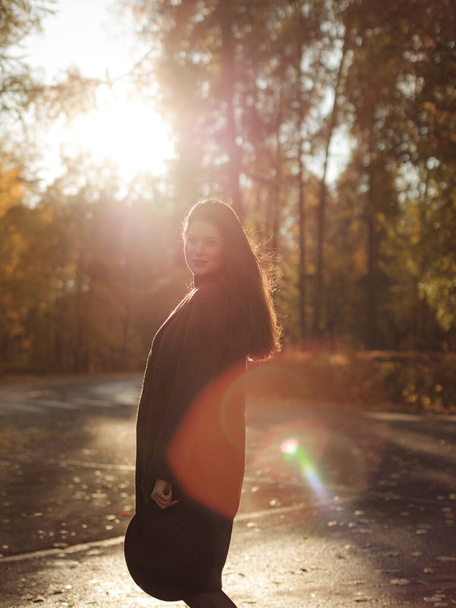 Young beautiful pregnant woman with dark hair in a black tight dress and coat posing on an autumn meadow in the park - Фото, зображення