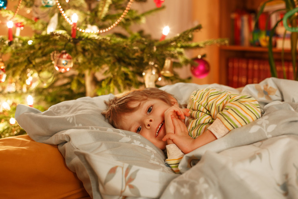 Pequeño niño rubio lindo durmiendo bajo el árbol de Navidad
 - Foto, imagen