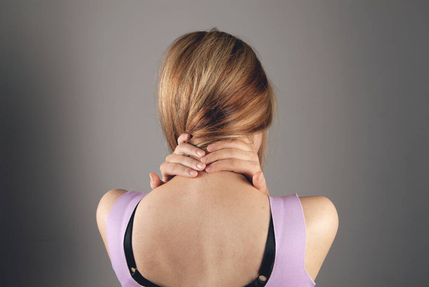 in a young woman, the back of her head hurts on a gray background - Photo, Image