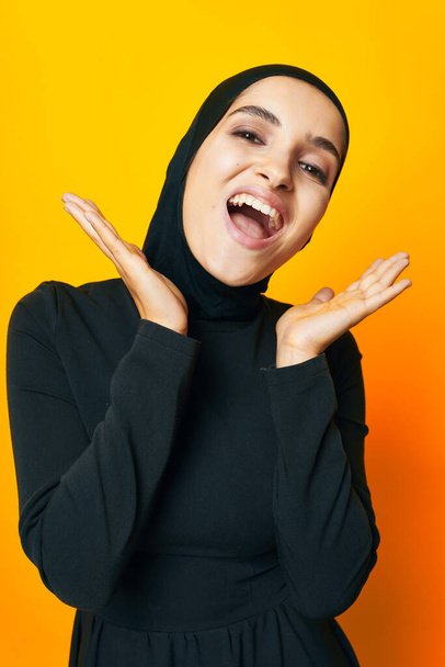 Muslim in black hijab posing fashion hand gesture yellow background - Foto, Imagen