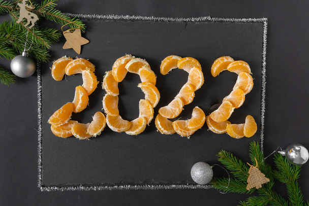 Közeleg a 2022-es újév. A számok vannak fektetve mandarin szeletek a fekete háttér, felső nézet. - Fotó, kép