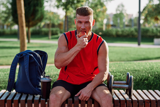 man in the park sits on a bench and eats an apple summer - Foto, immagini