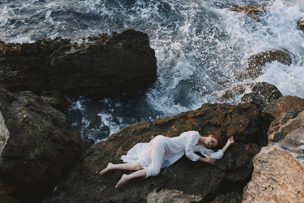 Frau im langen weißen Kleid nasse Haare auf einer Felswand liegend - Foto, Bild