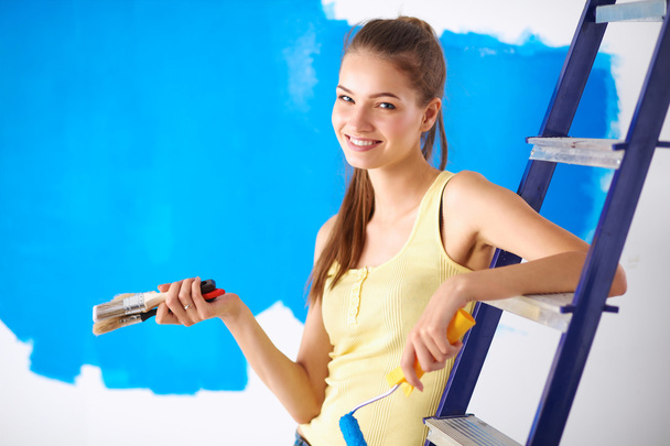 Happy beautiful young woman doing wall painting, sitting on ladder - Foto, Bild