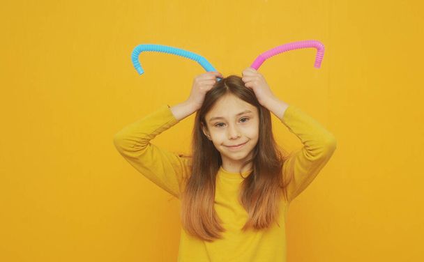 klein slim meisje in gele kleren speelt met trendy speelgoed pop tube - Foto, afbeelding