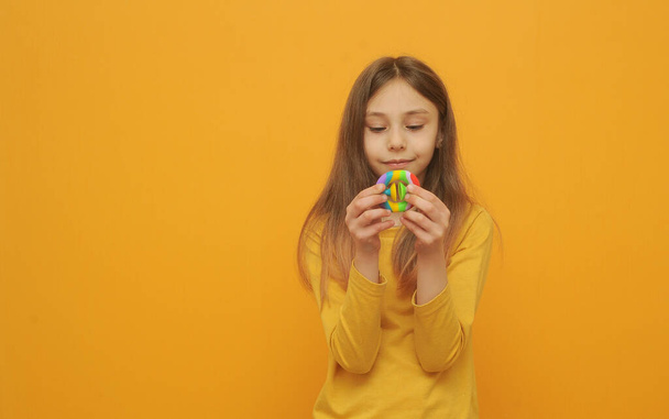 Kleine süße Mädchen spielen mit Pop-it auf gelbem Hintergrund. - Foto, Bild