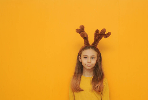 Petite fille drôle avec des oreilles de cerf posant sur fond coloré. Concept de vacances de Noël. - Photo, image