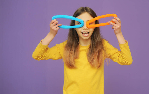 bambina intelligente in abiti gialli gioca con il tubo pop giocattolo alla moda - Foto, immagini