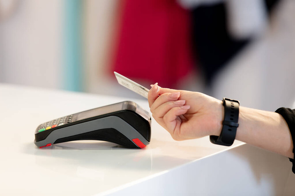 mano femenina sosteniendo una tarjeta pagando por los servicios a través de la terminal acostada sobre la mesa - Foto, imagen