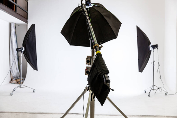 Empty photo studio with lighting equipment. Photographer workplace interior with professional tool set gear. Flash light white background scenes ready for studio shooting. Modern photographer studio - Photo, Image