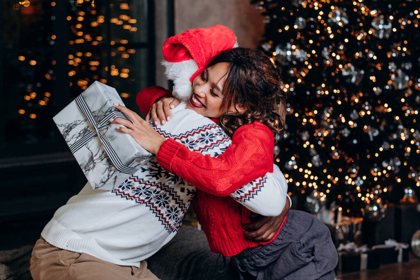 donna razza mista abbracciando l'uomo afro-americano con regalo di Capodanno sullo sfondo dell'albero di Natale, atmosfera di festa e la felicità degli amici di famiglia - Foto, immagini