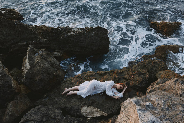 mujer en vestido blanco largo cabello mojado acostado en un acantilado rocoso naturaleza paisaje - Foto, Imagen
