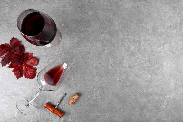 Vue du dessus des verres à vin rouge avec feuilles de raisin d'automne rouge et tire-bouchon et bouchon de vin sur table en pierre grise, concept vin rouge fond plat, espace de copie - Photo, image