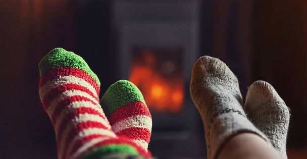 Two pair feet legs in winter wool socks at fireplace background. Couple family sitting at home on winter or autumn evening relaxing and warming up. Winter and cold weather concept, hygge Christmas eve - Foto, immagini