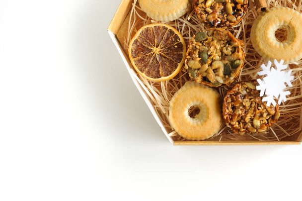 Biscuits aux noix et graines dans une boîte avec cannelle et orange et un flocon de neige sur fond blanc. Vue d'en haut. Copiez l'espace pour votre texte - Photo, image