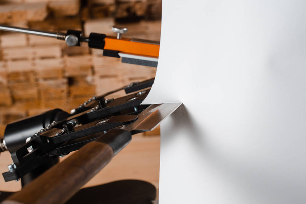 Proces van het snijden van papier met een scherp mes in de buurt van professionele messenslijper en een set van slijpstenen - Foto, afbeelding