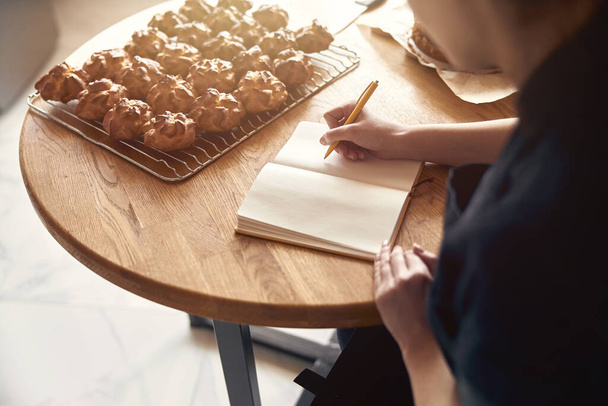Mujer profesional cocinera está escribiendo una receta de eclairs en la cocina moderna luz - Foto, imagen