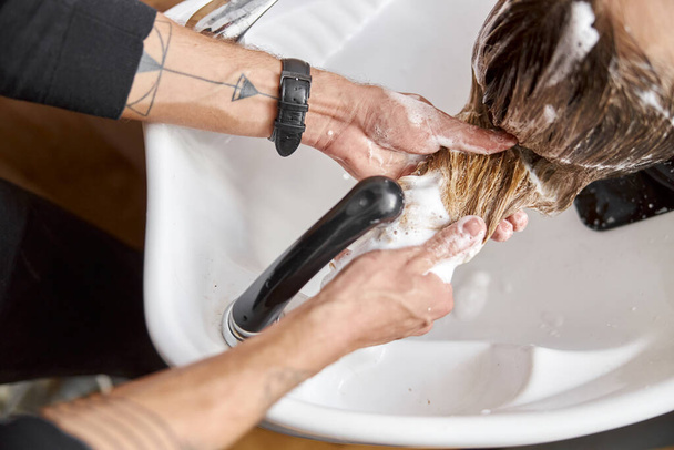 Selbstbewusste Stylistin wäscht im Salon Haare einer schönen kaukasischen Kundin - Foto, Bild