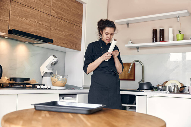 Genç, güzel, melez bir kadın açık modern mutfakta bir tabağa pasta kağıdı serer. - Fotoğraf, Görsel