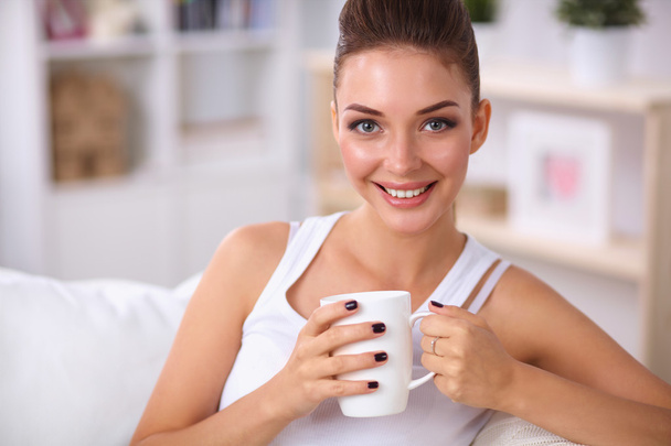 Young beautiful woman with a cup on sofa at home - Foto, Bild