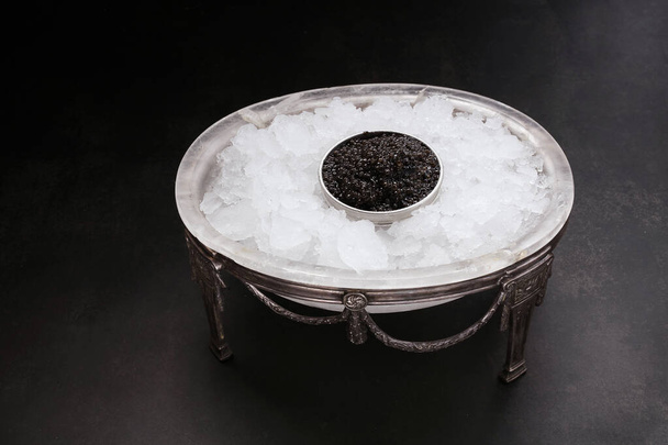 caviar in a metal box served in an antique caviar set with crushed ice on a dark background - 写真・画像