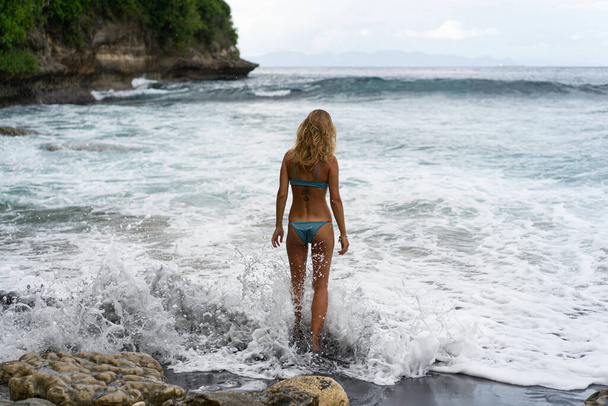 Beautiful young slender woman with long blond hair in a swimsuit on the beach near the ocean. Relax on the beach. Tropical vacations. - Foto, Imagen
