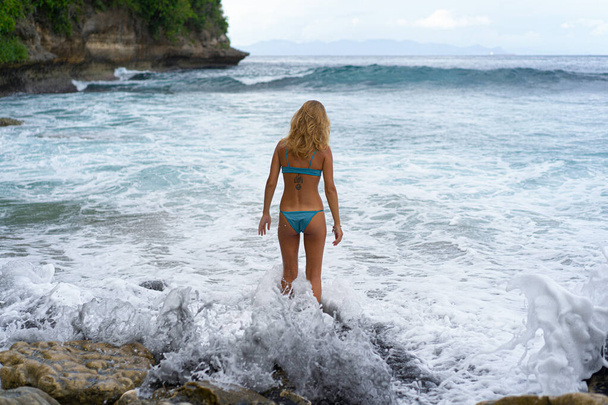 Красивая юная стройная женщина с длинными светлыми волосами в купальнике на пляже возле океана. Расслабься на пляже. Тропические каникулы. - Фото, изображение