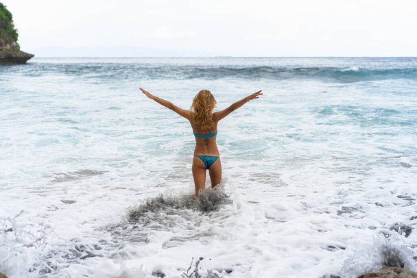 Beautiful young slender woman with long blond hair in a swimsuit on the beach near the ocean. Relax on the beach. Tropical vacations. - 写真・画像