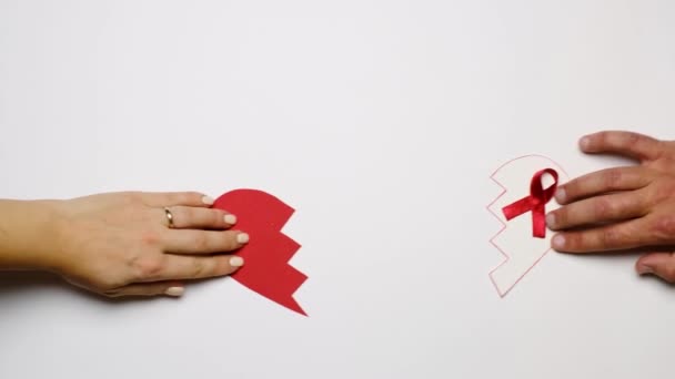Día Mundial de la Concienciación sobre el Sida. Las mitades del corazón con una cinta roja están conectadas en un todo: el concepto de cuidado, apoyo y amor de las parejas con el VIH. pareja casada cogida de la mano - Metraje, vídeo