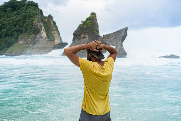 Νεαρός όμορφος γενειοφόρος ταξιδιώτης δίπλα στον ωκεανό. Παραλία Atuh, νησί Nusa Penida, Ινδονησία. Ταξιδιωτική ιδέα. Ινδονησία - Φωτογραφία, εικόνα