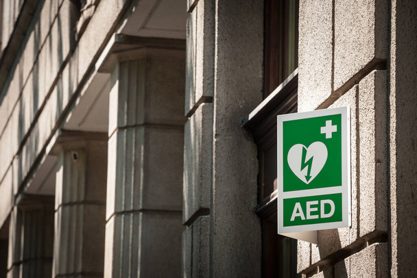 Logo elektrického defibrilátoru na ceduli v městském prostředí, které se řídí evropskými normami, označuje nedalekou přítomnost zařízení AED, povinnost vypořádat se se srdečními chorobami a infarkty - Fotografie, Obrázek