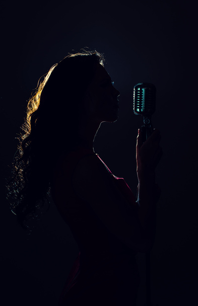 Silhouette of woman singing into vintage microphone. - Photo, Image