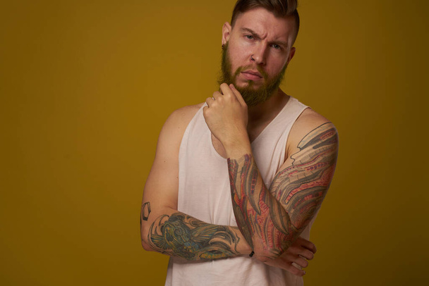 bearded man in white t-shirt with tattoos on his arms posing serious look - Foto, Imagen