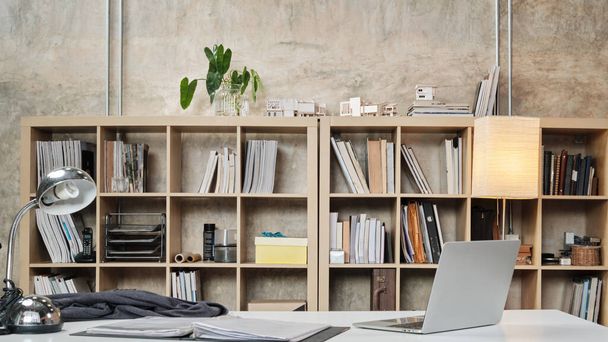 No people in a casual workplace, desk, and president chair in Architecture and Interior Design office, models, books, accessories, and equipment in the bookshelf decorate in modern-loft style. - Фото, зображення