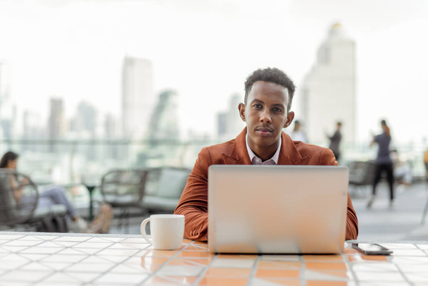 Portrait of African businessman outdoors in coffee shop using laptop computer - Foto, imagen