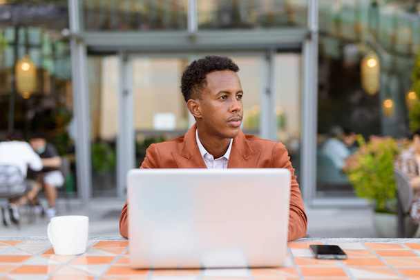 Portrait d'un homme d'affaires africain à l'extérieur dans un café en utilisant un ordinateur portable - Photo, image
