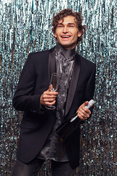 Holidays concept - happy tipsy man with bottle of champagne and wine glass at christmas or new year party on a sparkle background. - Фото, изображение