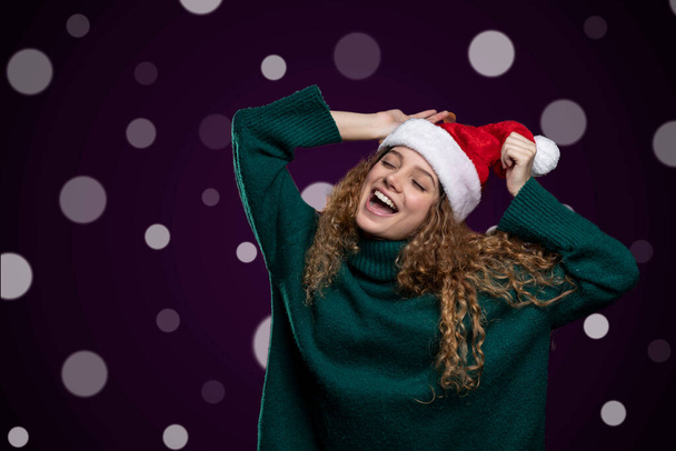 nuori nainen tekee onnellisia ilmaisuja yllään jouluhattu ja joulu pusero, valot taustalla - Valokuva, kuva