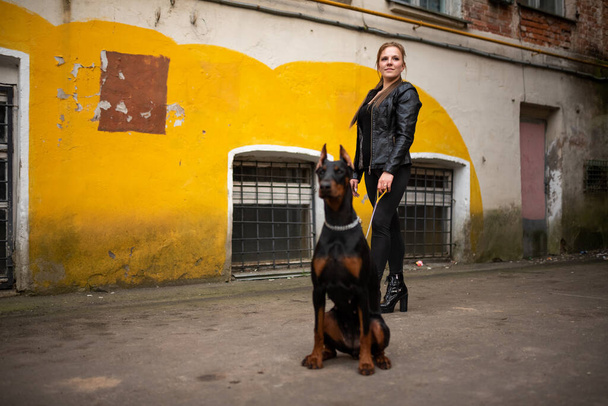 A girl in leather, with a Doberman, in an old yard. - Fotografie, Obrázek
