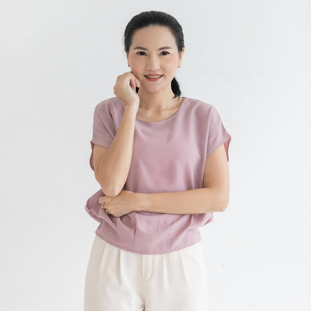 Portrét detailní studio záběr asijské mladé šťastný přátelský krásný žena modelu v ležérní růžová outfit stojící s úsměvem při pohledu na fotoaparátu držet ruku na bradě zkřížené rameno v přední bílé zdi pozadí. - Fotografie, Obrázek