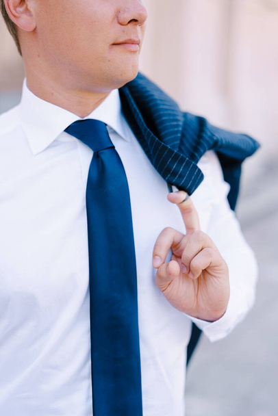 Man in a white shirt holds a jacket hanging on his shoulder with his finger - Photo, Image